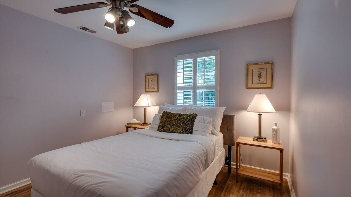A bedroom with a bed, two bedside tables, a ceiling fan, and a window with blinds.