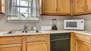 Una cocina con armarios de madera, encimera blanca, un fregadero, microondas y lavavajillas.