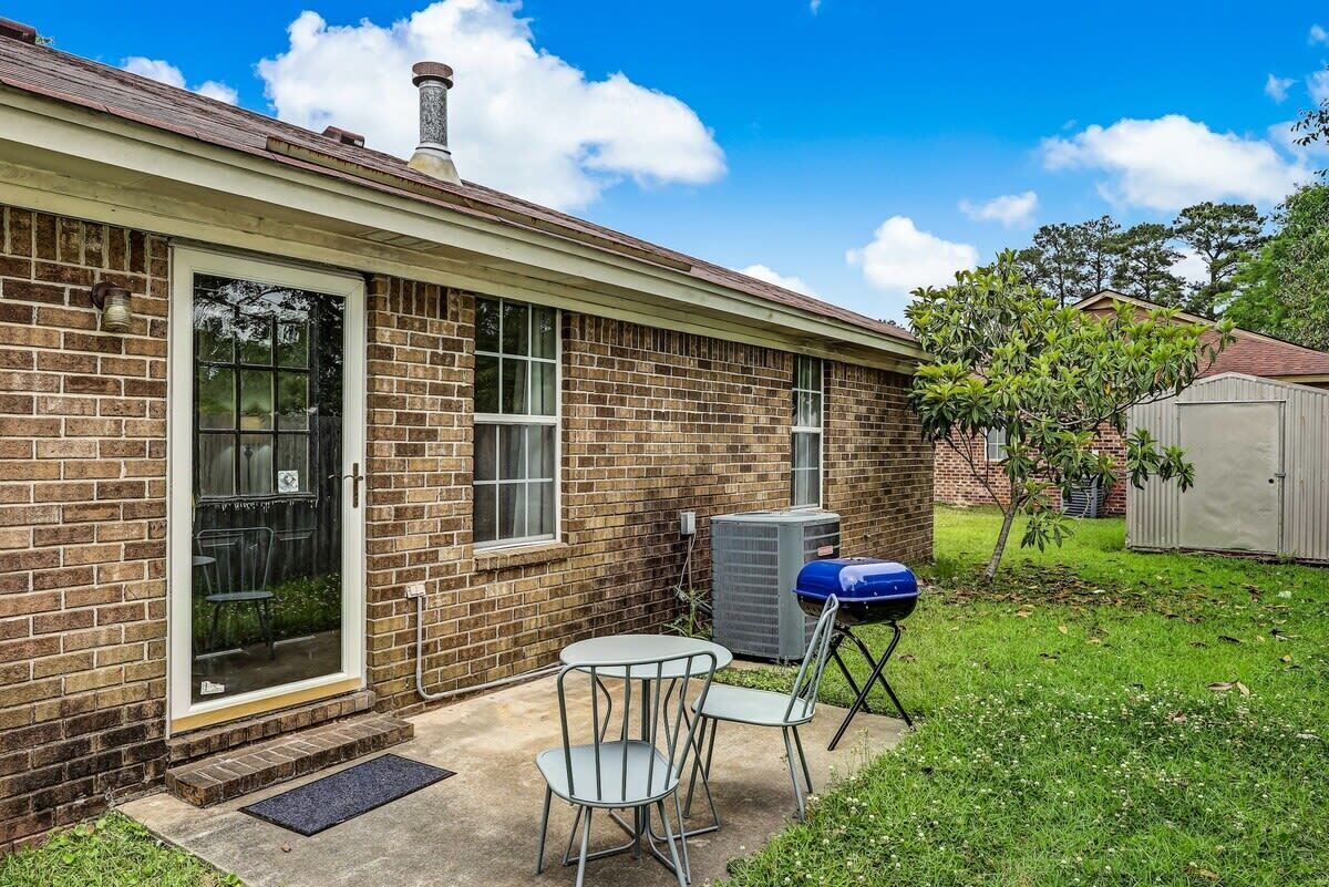 Une maison de plain-pied en briques, avec une porte d’entrée, un petit patio doté d’une table et de chaises, et un barbecue bleu.