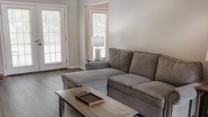 Un salon comprenant un canapé d’angle, une table basse en bois et une porte à panneaux de verre.