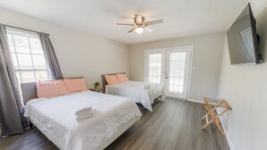 Une chambre avec deux lits, un ventilateur de plafond, une télévision et un étendoir en bois.