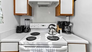 Cocina compacta con estufa blanca, hervidor, cafetera y licuadora.