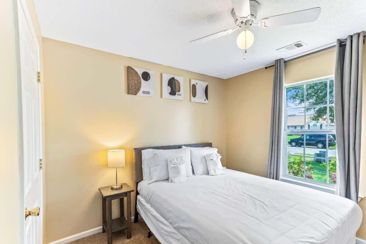 A hotel room with a bed, a nightstand, a ceiling fan, and a window with a view of the outside.