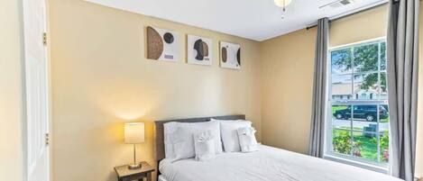 A hotel room with a bed, a nightstand, a ceiling fan, and a window with a view of the outside.