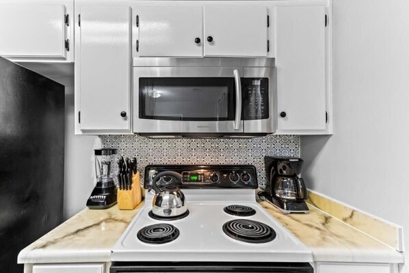 A compact kitchen with a microwave, stove, and coffee maker. - Screened Porch, Firepit, Patio! Peaceful in Pooler (Pooler)