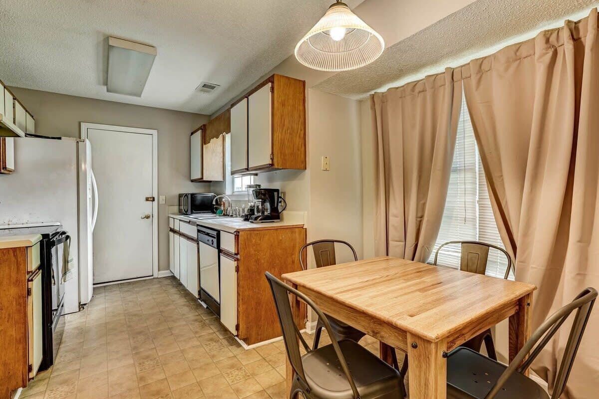 A compact kitchen with a wooden table and chairs, a refrigerator, a stove, and a microwave.