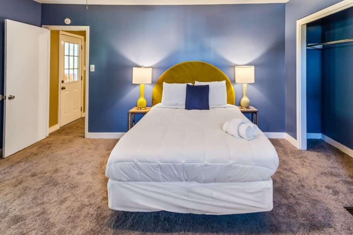 Cama bem arrumada com lençóis brancos em quarto com paredes azuis e piso coberto por carpete.