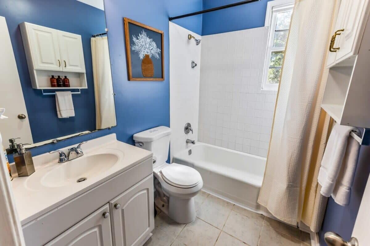 Een badkamer met een witte wastafel, toilet en badkuip, blauwe wanden en een ingelijst foto aan de muur.