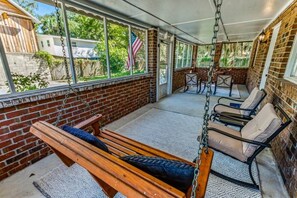 A covered patio with a swing, cushioned chairs, and a table. - Fenced Yard, Ping Pong & BBQ Grill Near Downtown (Savannah)