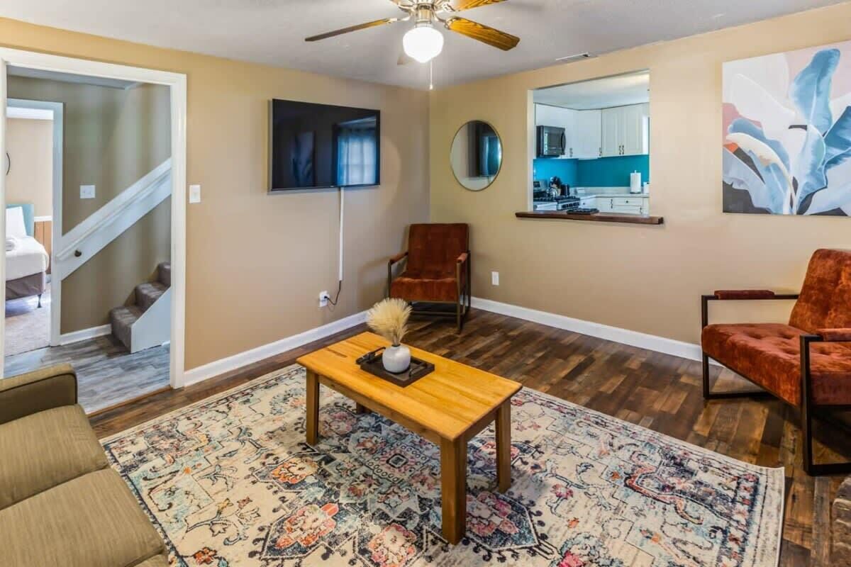 Una sala de estar con una mesa de centro de madera, un tapete estampado, un sillón rojo y un ventilador de techo.