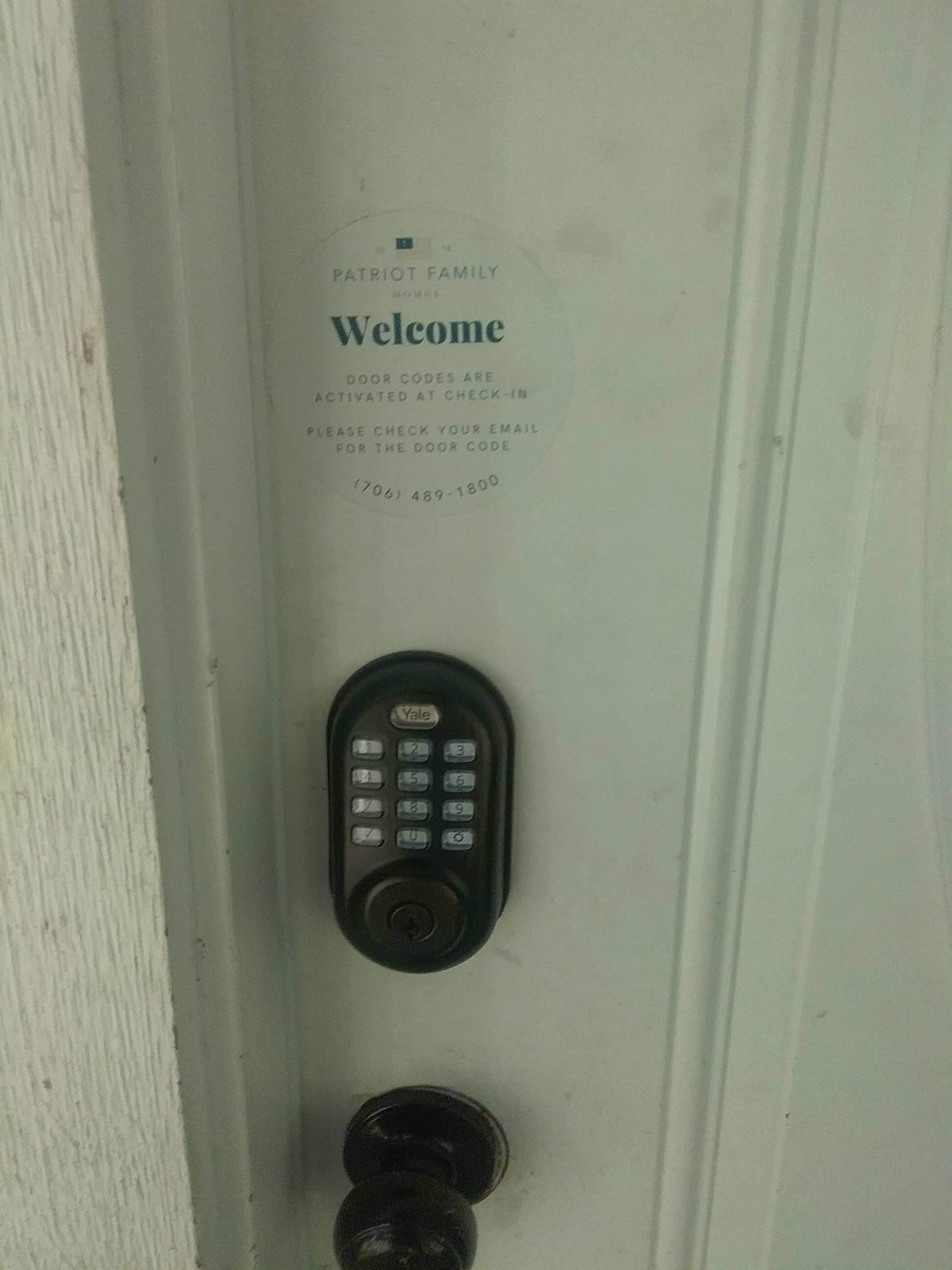 Puerta con teclado electrónico y letrero que dice 'Patriot Family Welcome' con instrucciones para el registro por correo electrónico.