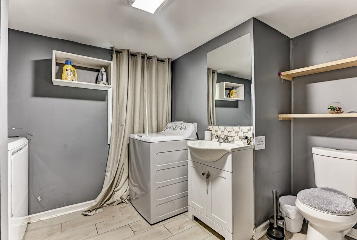 A compact bathroom with a washing machine, a sink, and a toilet.