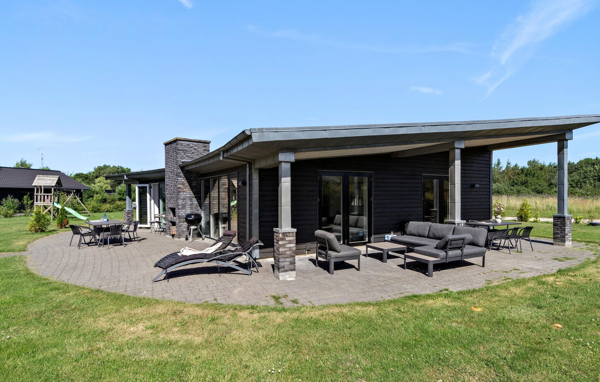 A modern outdoor patio with a covered seating area, a barbecue grill, and a stone fireplace.