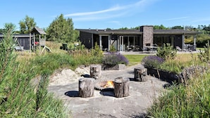 A modern house with a patio area featuring a fire pit, outdoor seating, and a barbecue grill. - Awesome home in Glesborg with sauna (Glesborg)