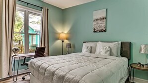 Ein Schlafzimmer mit einem großen Bett, einem Schreibtisch mit Stuhl, einer Lampe und einem Fenster mit Vorhängen.