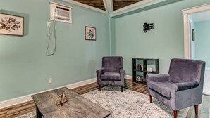 Ein Wohnzimmer mit türkisfarbenen Wänden, Holzboden und zwei grauen Sesseln, einem Holztisch und einem gemusterten Teppich.