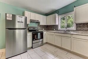 A kitchen with white cabinets, a stainless steel refrigerator, a stove, and a window with a view of greenery.