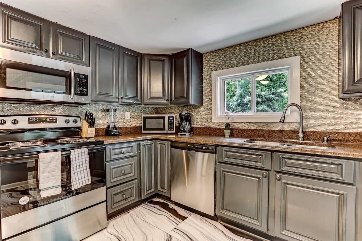 A modern kitchen with dark cabinets, stainless steel appliances, and a stone backsplash.