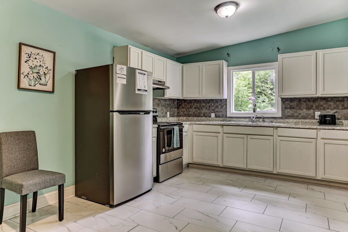 A kitchen with white cabinets, a stainless steel refrigerator, an oven, and a window.