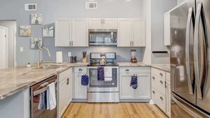 A modern kitchen with white cabinets, stainless steel appliances, a marble countertop, and pendant lighting.