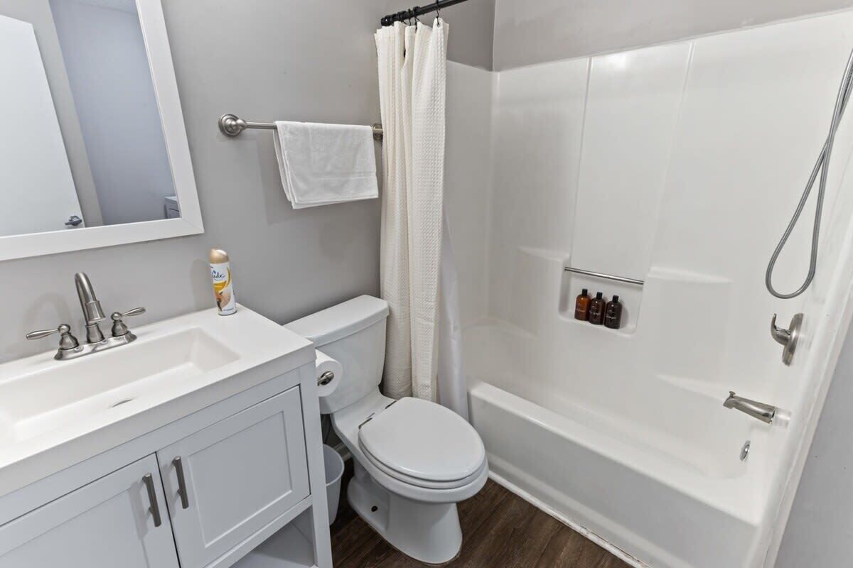 A bathroom with a white sink, toilet, and bathtub. There is a shower curtain, a towel rack, and a mirror above the sink.