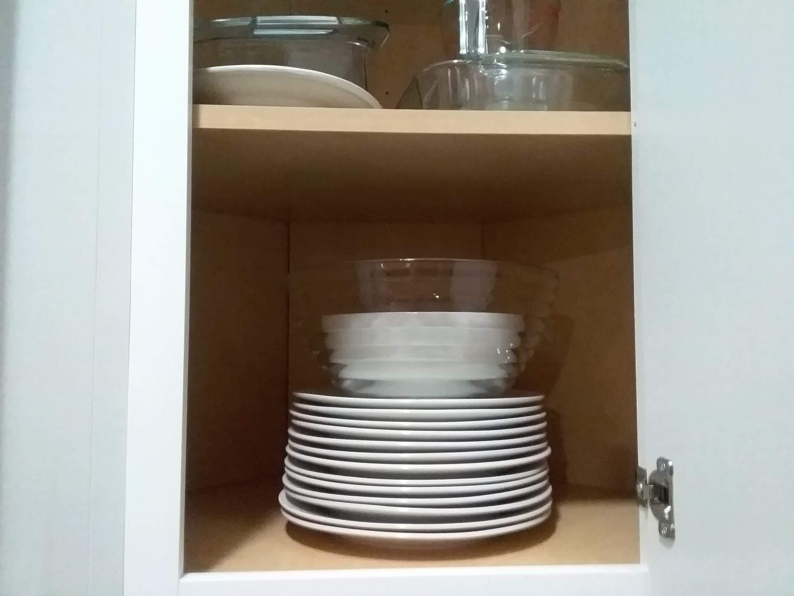 Ein Schrank mit einer Reihe weißer Teller und einem durchsichtigen Glasbehälter.