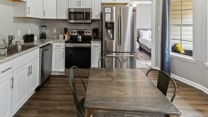 A modern kitchen with white cabinets, stainless steel appliances, and a wooden dining table. - Fenced Yard & BBQ Grill Near Dining, Parks & Shops (Savannah)