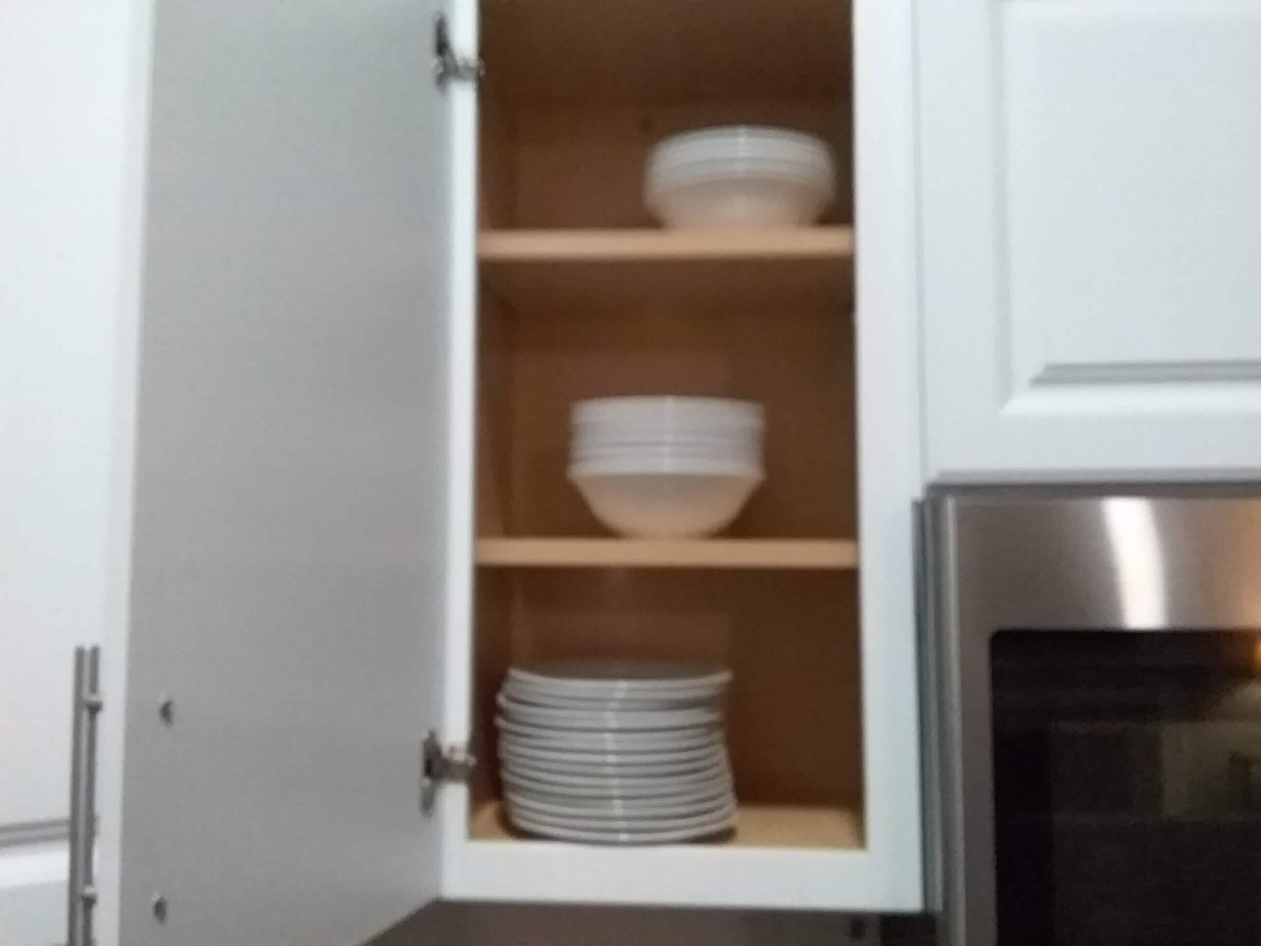 Una cocina con armarios blancos, horno de acero inoxidable y estantes con cuencos y platos blancos.