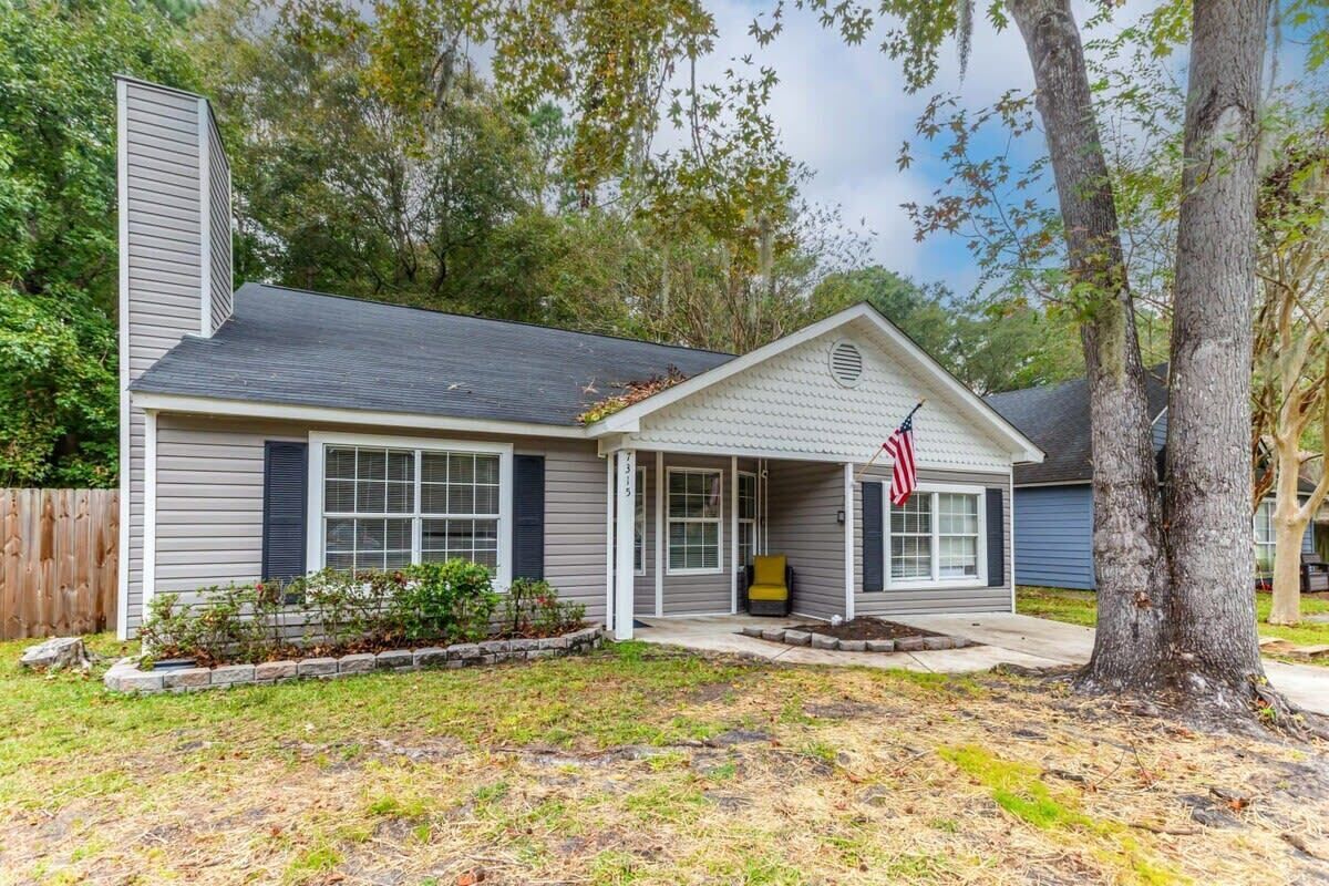 A single-story house with a front porch, a small garden, and an American flag.