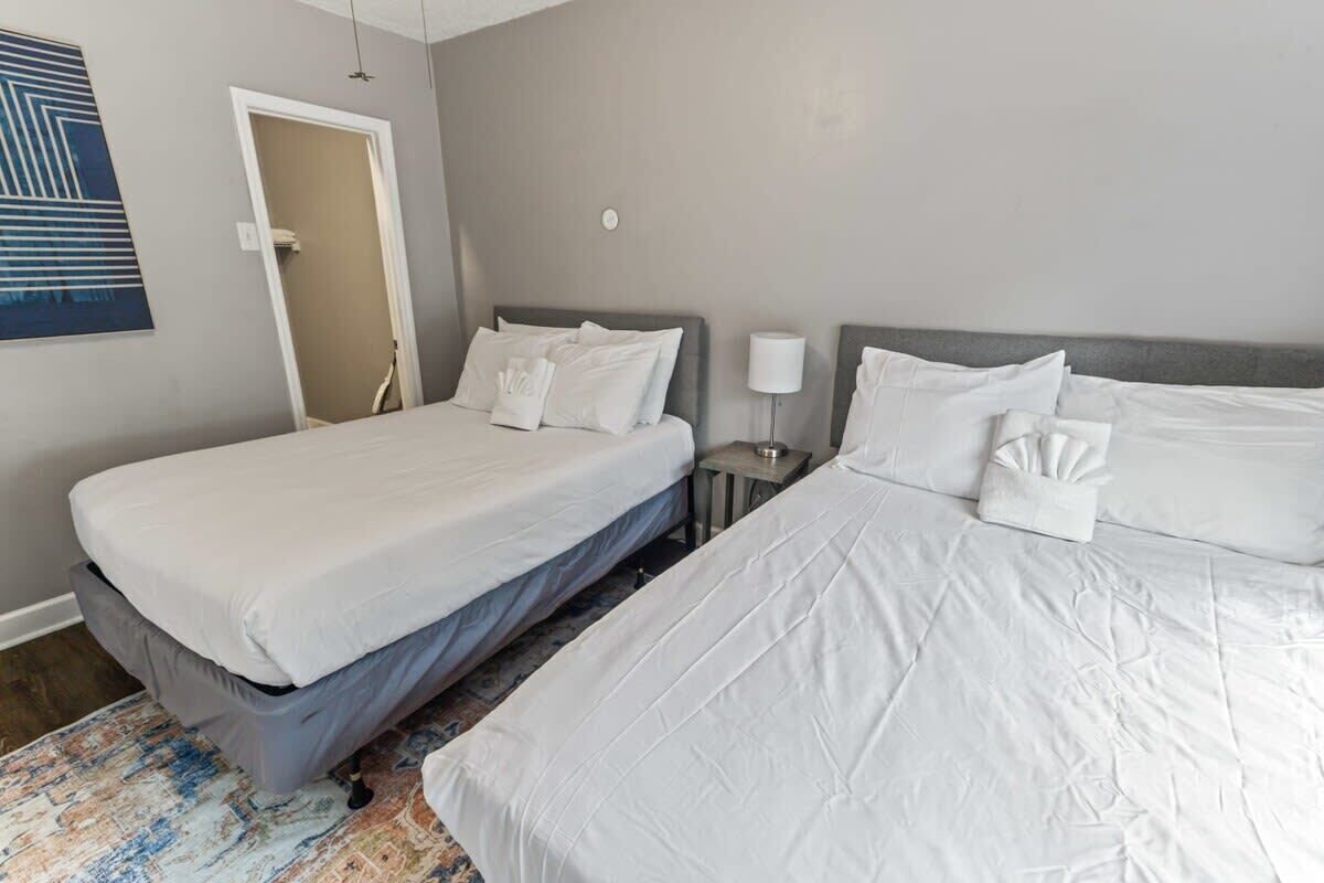Ein Hotelzimmer mit zwei Betten, einem kleinen Nachttisch mit Lampe und einer Tür zu einem Badezimmer.