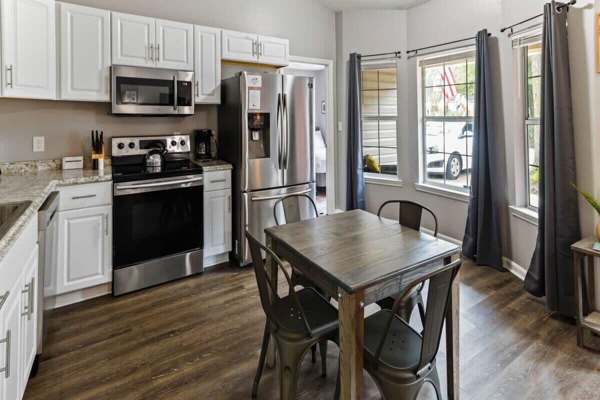 A modern kitchen with white cabinets, stainless steel appliances, and a wooden dining table.