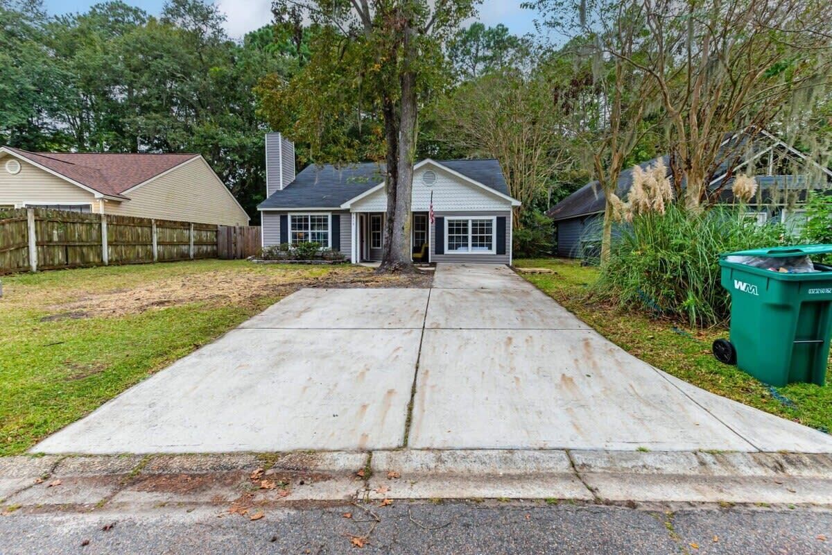A residential driveway leading to a house with a garage, surrounded by a wooden fence and trees.
