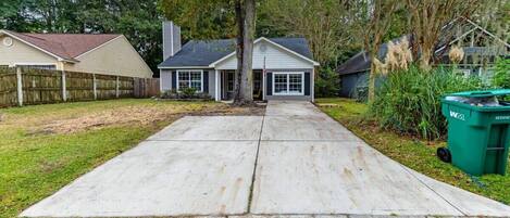 A residential driveway leading to a house with a garage, surrounded by a wooden fence and trees.