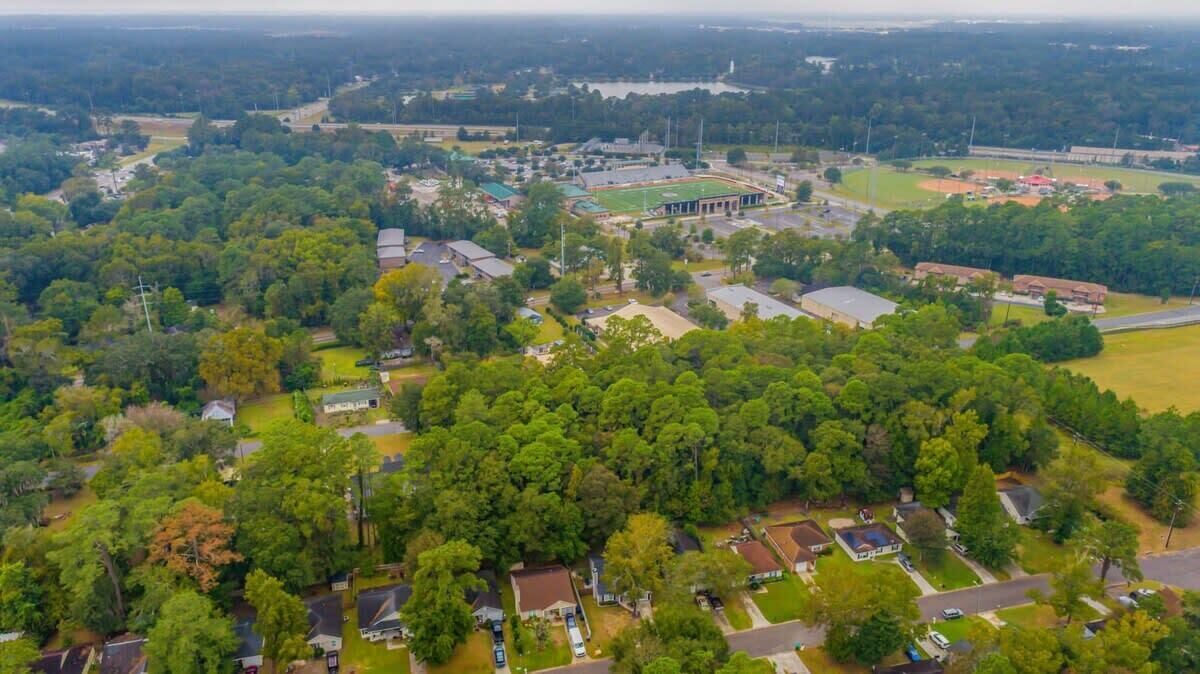 An aerial view of a residential area with houses, a large building with a green roof, and a sports field.