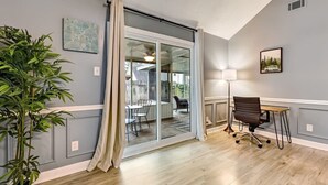 Ein Zimmer mit einer Schiebetür zu einer Terrasse, einem Schreibtisch mit Stuhl, einem Blumentopf und einem gerahmten Bild an der Wand.