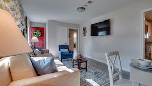 A living room with a sofa, a blue armchair, a coffee table, and a TV mounted on the wall.