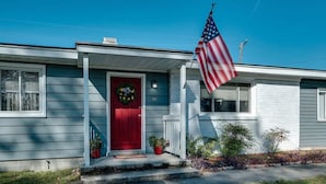 A single-story house with a red front door, white porch railing, and a small front yard.
