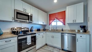 A modern kitchen with white cabinets, stainless steel appliances, and a window with a red curtain.