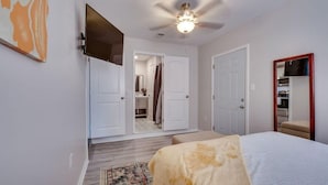 A bedroom with a bed, a ceiling fan, a TV mounted on the wall, and a door leading to a bathroom.