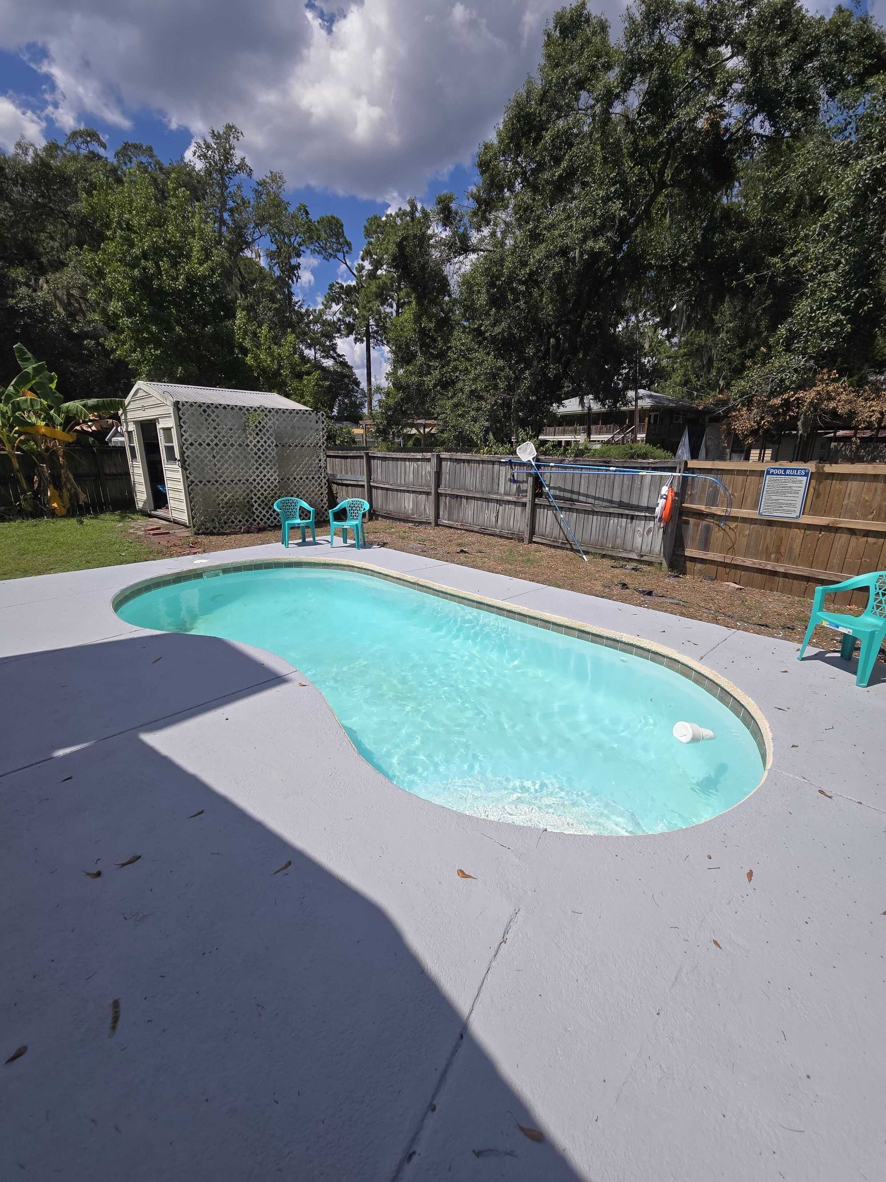 Una piscina con muelle de madera, rodeada por una valla de madera y árboles.