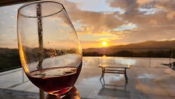 A glass of red wine held by a hand, with a sunset view through a glass roof. - Magic Place Monteverde  (Monteverde)