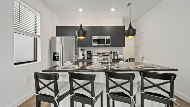Une cuisine moderne avec un îlot central, des chaises noires et des luminaires suspendus.