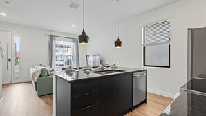 Une cuisine moderne dotée d’un îlot central, de meubles de rangement noirs et de luminaires suspendus.