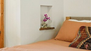 Quarto com cama, uma prateleira de madeira com um vaso de flores e um cobertor estampado na cama.