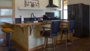 A kitchen with a wooden island, bar stools, a ceiling fan, a refrigerator, and a window. - Sequoia Luxury Ranch House, View, Pool, horses, 30 min to Park, in Foothills (Exeter)