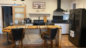 A modern kitchen with a central island, bar stools, a black refrigerator, and a coffee machine. - Sequoia Luxury Ranch House, View, Pool, horses, 30 min to Park, in Foothills (Exeter)