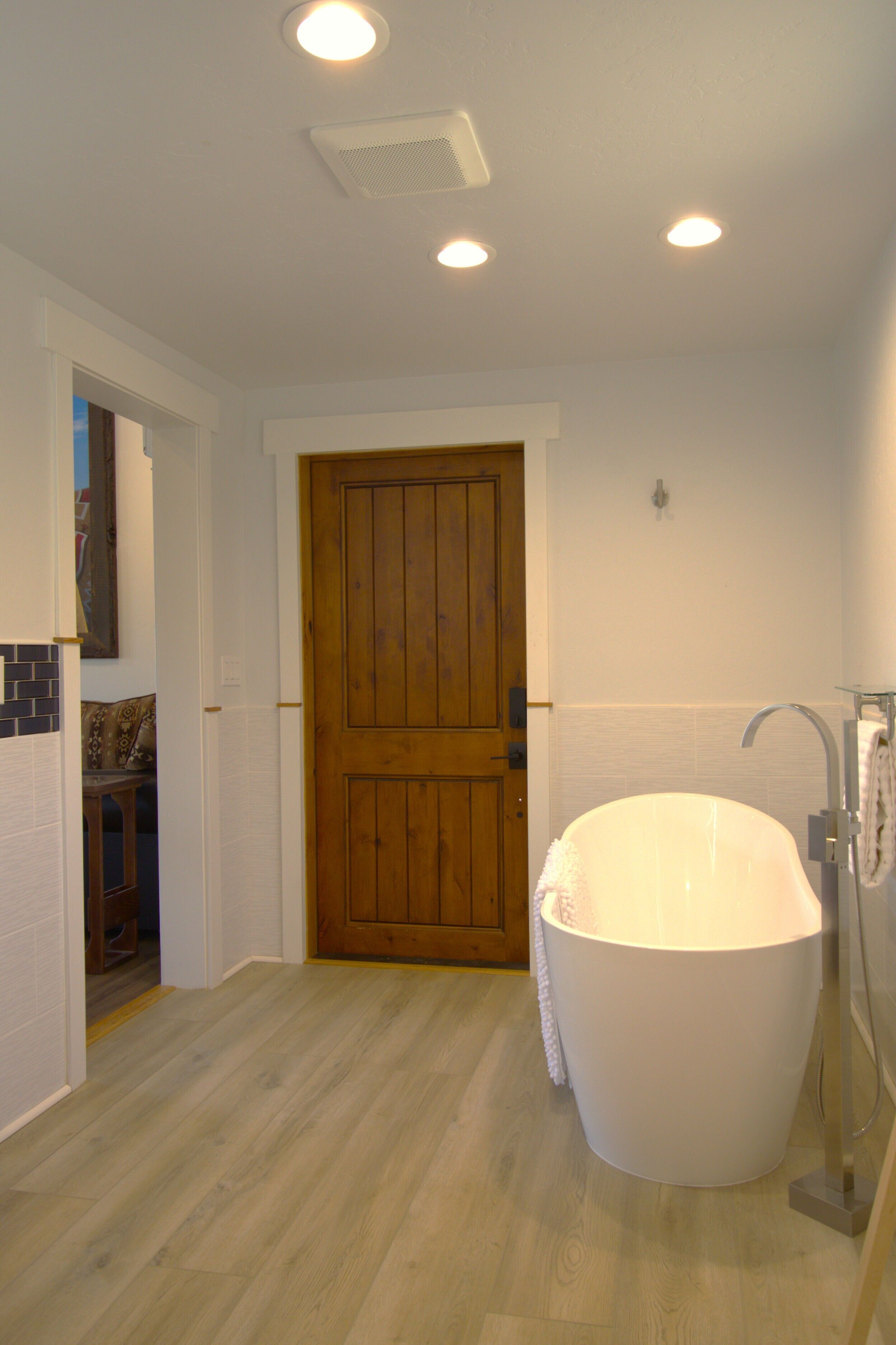 A bathroom with a wooden door, a white bathtub, and a shower area.