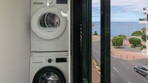 A view of a washing machine and dryer stacked in a room with a window overlooking a street and ocean. - Promenade II – Comfort and Elegance in Funchal (Funchal)