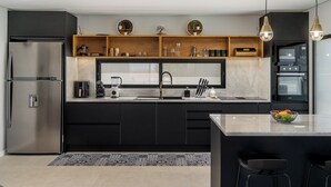 Una cocina moderna con armarios negros, un refrigerador de acero inoxidable, un horno empotrado y un estante de madera con utensilios de cocina.