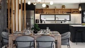 Una cocina moderna con una isla central, estantes de madera y un comedor con sillas grises tapizadas.
